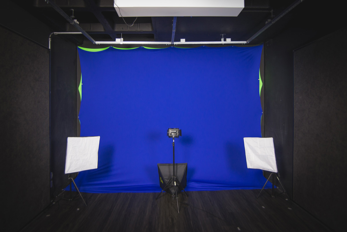 Foto de um estúdio com um fundo azul no centro; dois softbox nos lados esquerdo e direito da sala e um rebatedor no centro, com uma câmera sobre um tripé apontada para o fundo azul