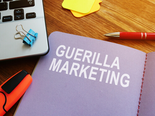 Imagen de una plantilla con la frase marketing de guerrilla, al costado algunos materiales de escritorio y una notebook.