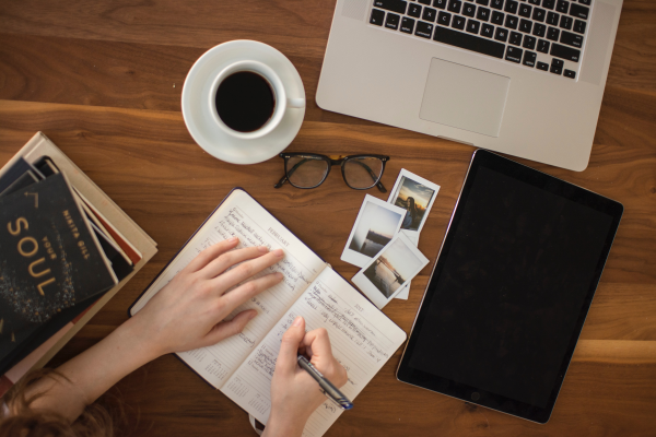 Imagen de una notebook junto a un bloc de notas una taza de café y un celular, representando la educación y los cursos en línea.