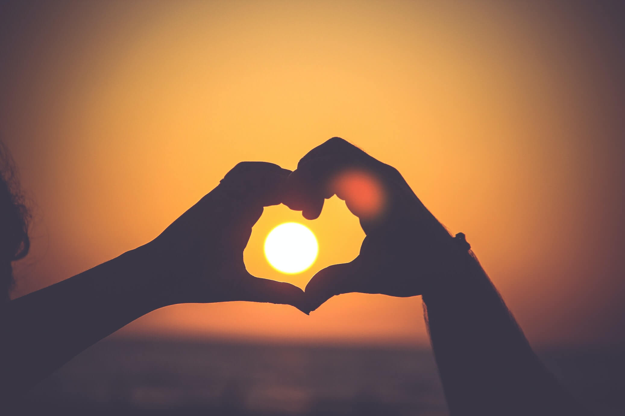 Image of two hands creating a heart shape at a sunset