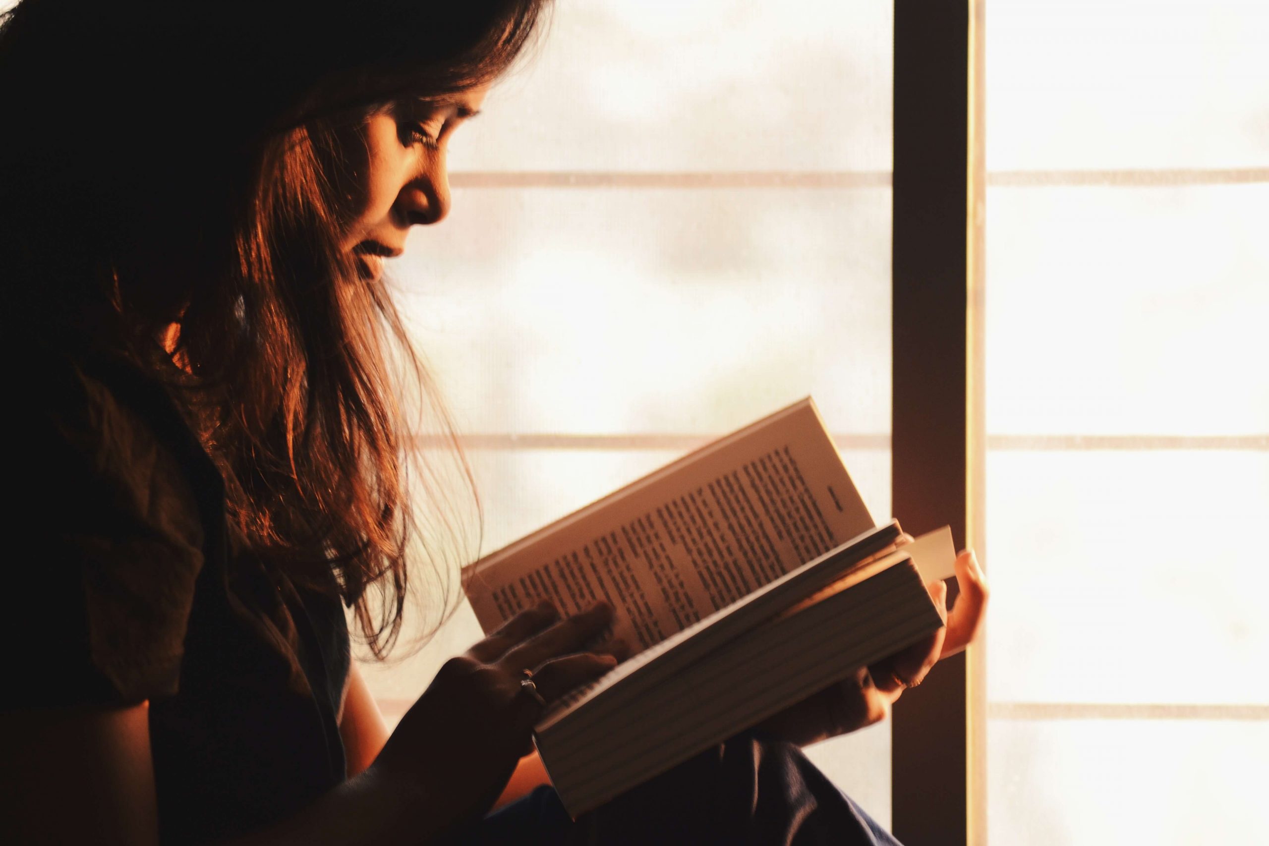 Imagen de una mujer leyendo un libro con luz ténue.