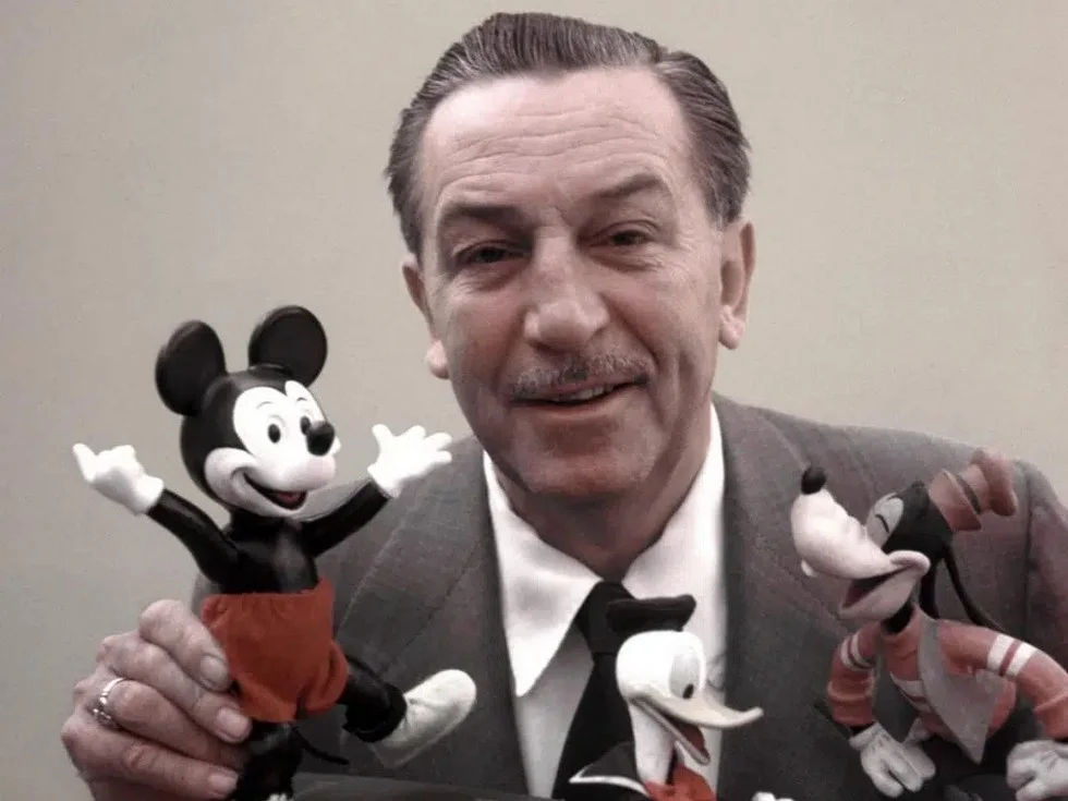 Fotografía del empresario y emprendedor Walt Disney. y en sus manos dos muñecos, Mickey y Goofy.