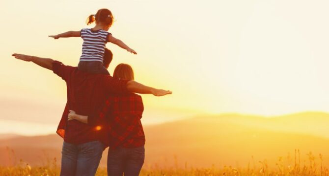 imagens chamativas - foto de um homem com uma criança nos ombros e uma mulher ao lado. todos de braços abertos de frente a um por do sol