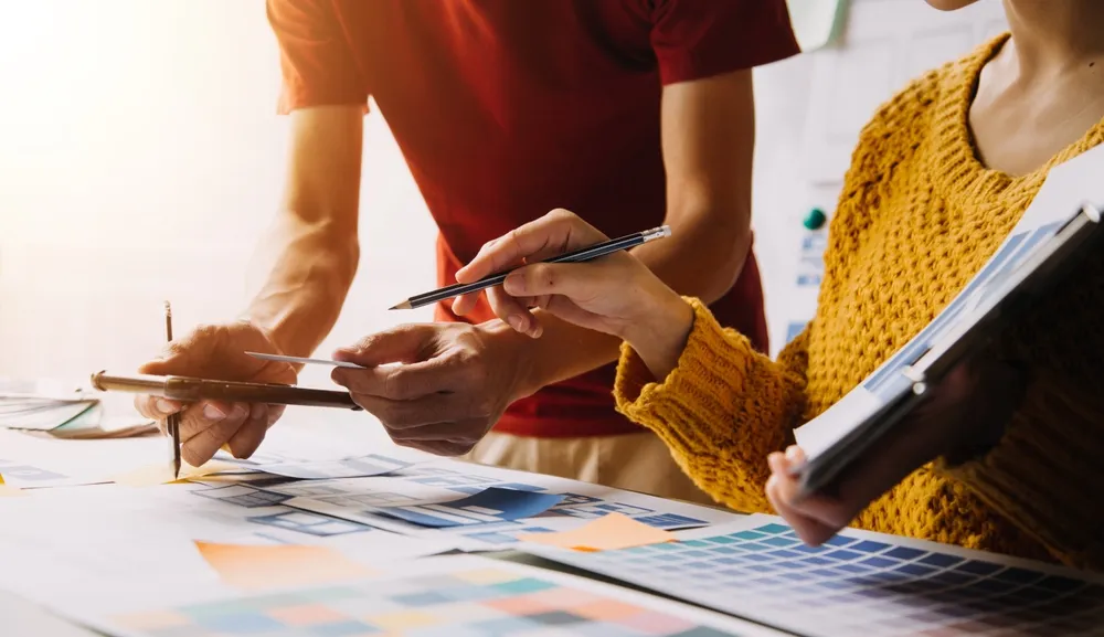 Dos personas analizan muestras de color y bocetos mientras planifican una estrategia de marketing