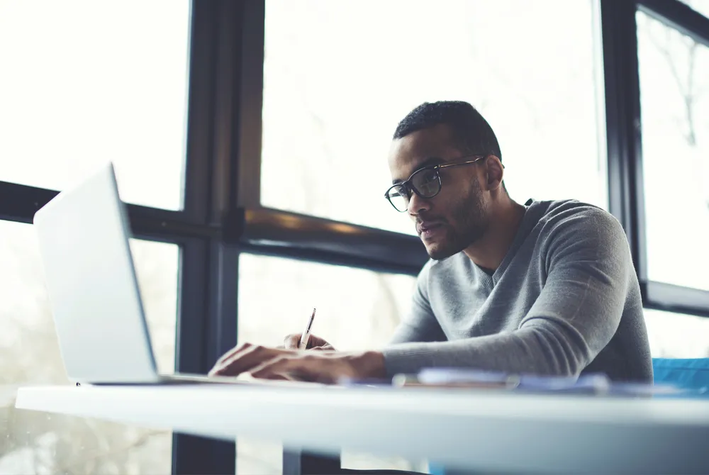 Professional working on a laptop and taking notes at a desk