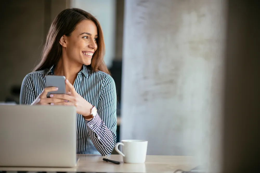 Smiling woman using her phone at a desk, thinking about what to sell to make money