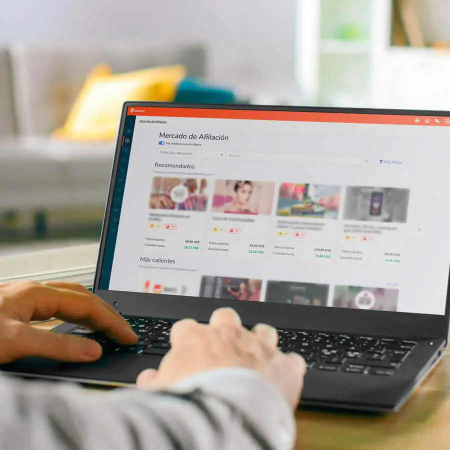 Hands typing at a laptop. On the screen, there is a page showing Hotmart Marketplace with courses to buy.