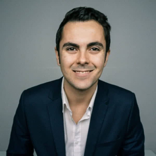 Hombre con camisa blanca y chaqueta oscura sonriendo.