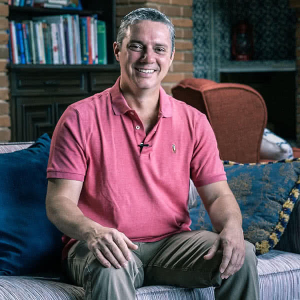 Hombre sonriente con blusa rosa sentado en un sillón.