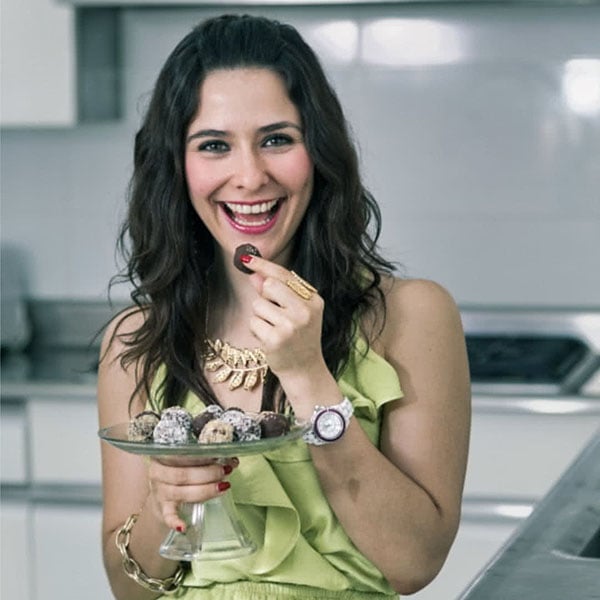 Mujer de cabello oscuro con traje verde sosteniendo dulces en una bandeja.