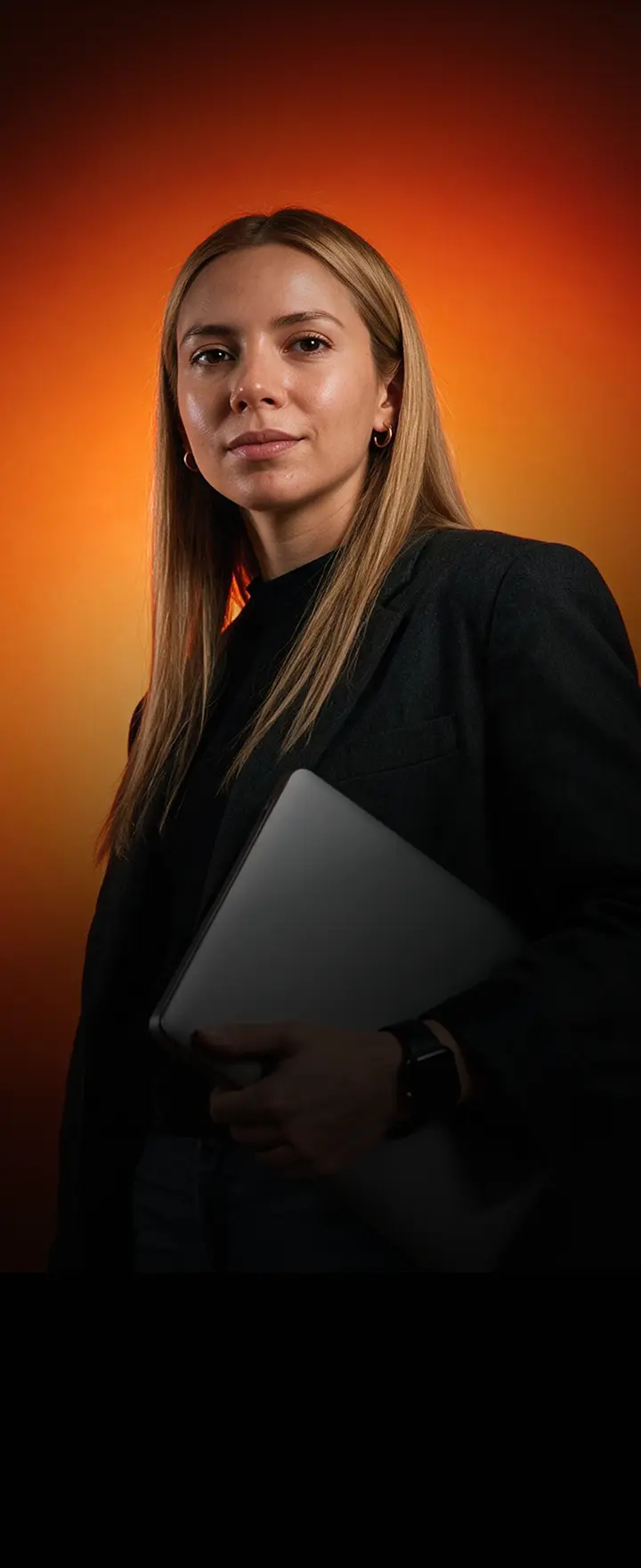 Mujer profesional posa con su laptop bajo una luz naranja intensa, imagen que representa a quienes emprenden con Hotmart Colombia.