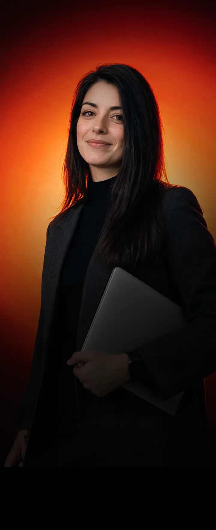 Portrait d'une créatrice tenant son ordinateur portable devant un fond orange, symbole des infopreneurs qui développent leurs produits digitaux avec Hotmart France.