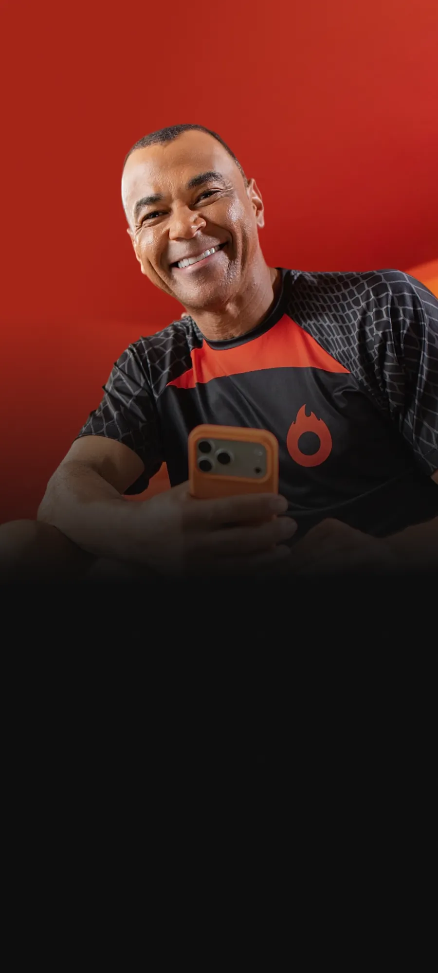 Cafu sorrindo em arquibancada laranja segurando celular